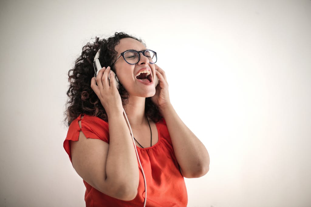 Eine energiegeladene Frau in einem roten Oberteil genießt Musik mit Kopfhörern und schließt vor Freude die Augen, da sie sich mit ihrer Stimme wohlfühlt.