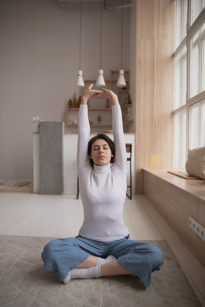 Frau sitzt in einer Yoga-Position und streckt die Arme in einer ruhigen Umgebung nach oben.